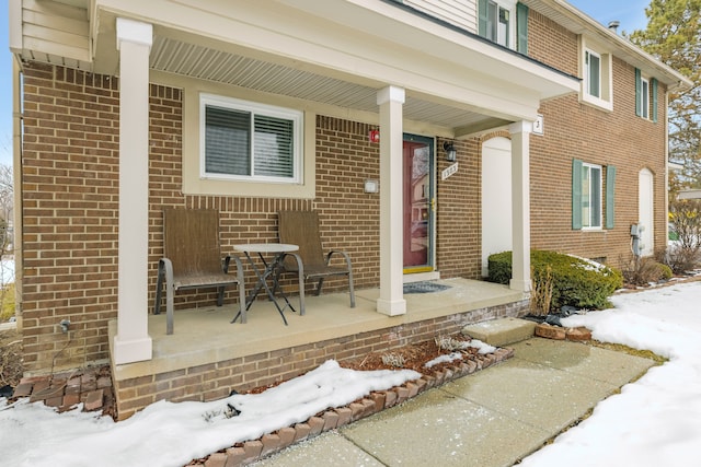 snow covered property entrance with covered porch and brick siding