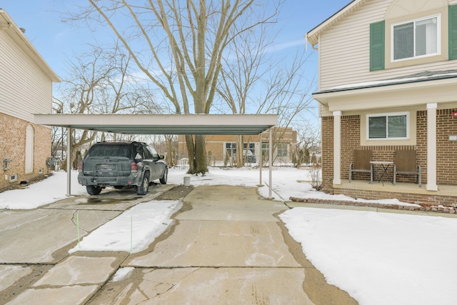 snow covered parking area featuring a carport and concrete driveway