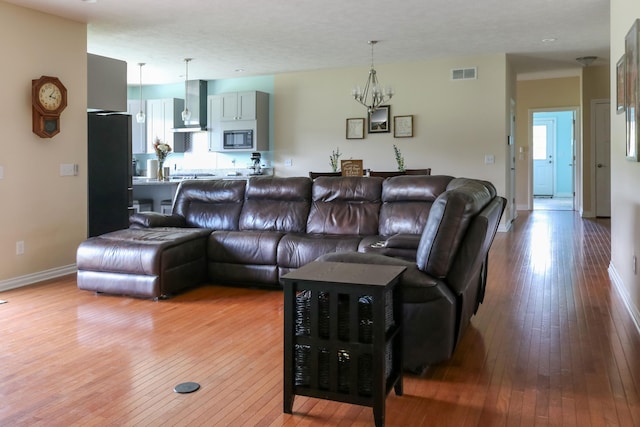 living room with visible vents, a notable chandelier, baseboards, and wood finished floors