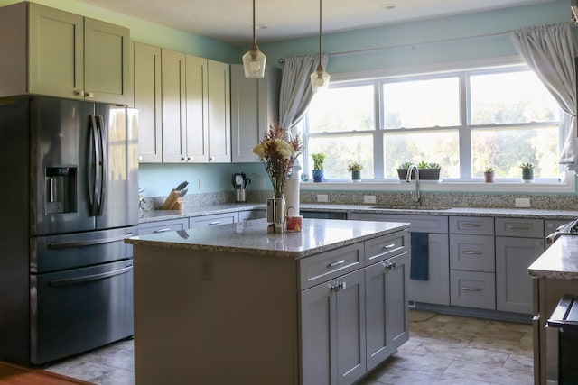 kitchen with stainless steel fridge with ice dispenser, a kitchen island, light stone counters, hanging light fixtures, and a sink