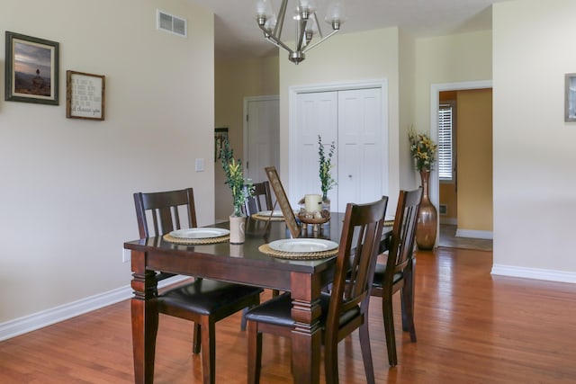 dining space featuring baseboards, visible vents, a chandelier, and wood finished floors