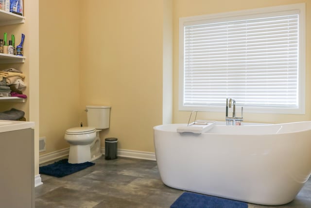 bathroom featuring a soaking tub, baseboards, and toilet