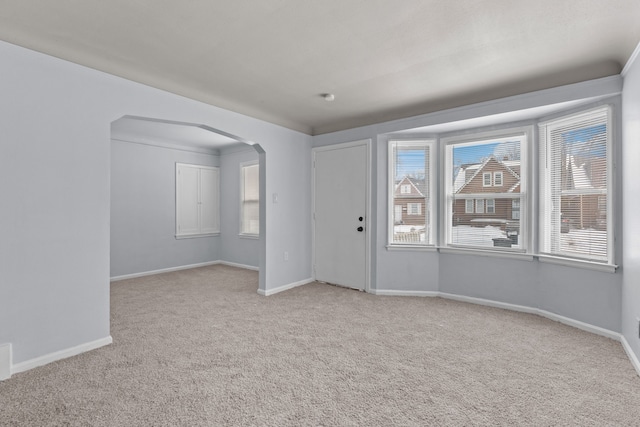 foyer entrance featuring arched walkways, light carpet, and baseboards