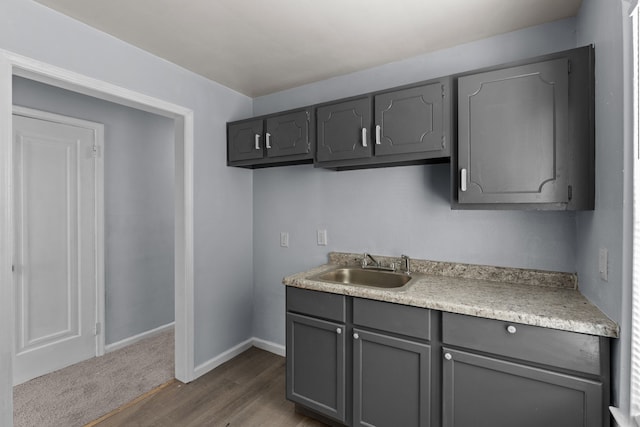 kitchen with baseboards, light countertops, a sink, and gray cabinetry