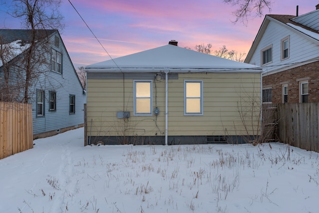 snow covered back of property featuring crawl space, a chimney, and fence