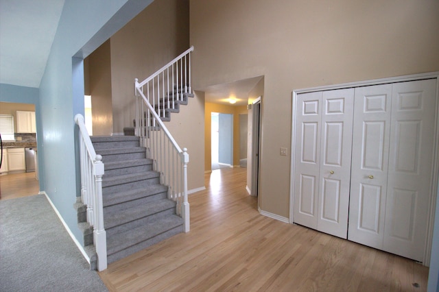 stairway featuring a high ceiling, baseboards, and wood finished floors