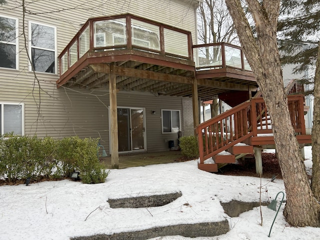 snow covered back of property featuring brick siding, a deck, and stairs