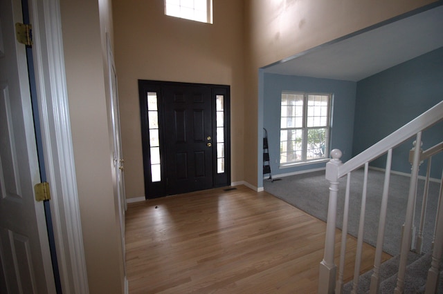 foyer with a high ceiling, light wood-style flooring, stairs, and baseboards