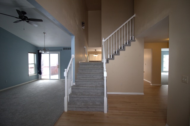 stairway with high vaulted ceiling, baseboards, visible vents, and ceiling fan with notable chandelier