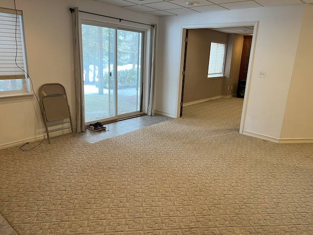 unfurnished room with baseboards, a drop ceiling, and light colored carpet