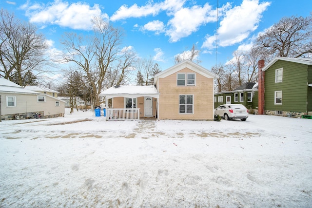 snow covered back of property featuring covered porch