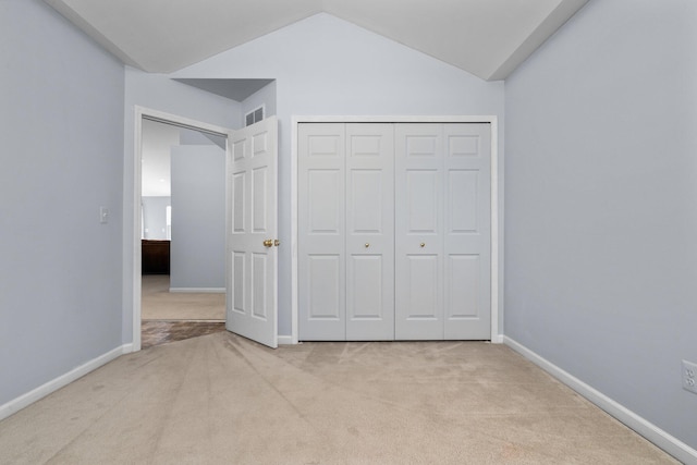 unfurnished bedroom featuring a closet, visible vents, light carpet, vaulted ceiling, and baseboards