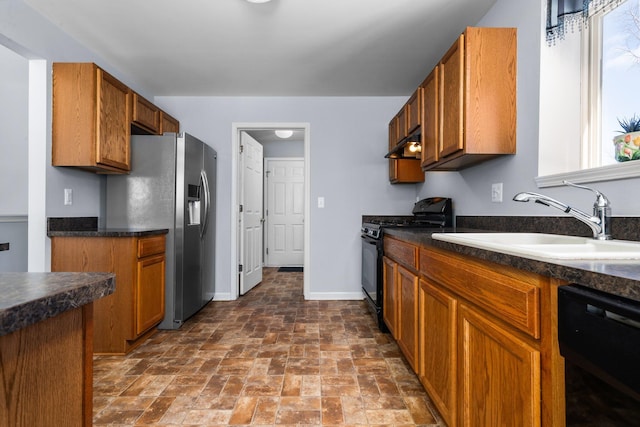 kitchen featuring dark countertops, a sink, black appliances, under cabinet range hood, and baseboards