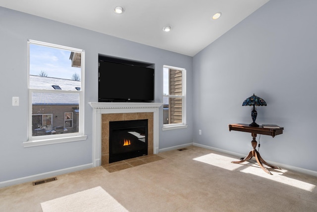 living area with a tile fireplace, visible vents, vaulted ceiling, and light carpet