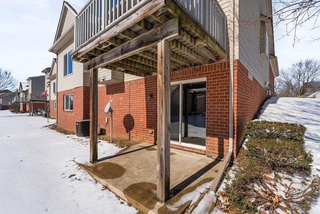 snow covered property featuring brick siding, a balcony, and central air condition unit