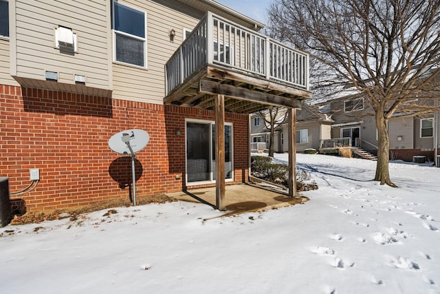 snow covered back of property with cooling unit, brick siding, and a balcony