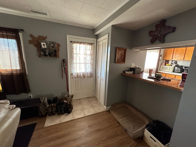 foyer entrance featuring light wood finished floors, visible vents, and ornamental molding