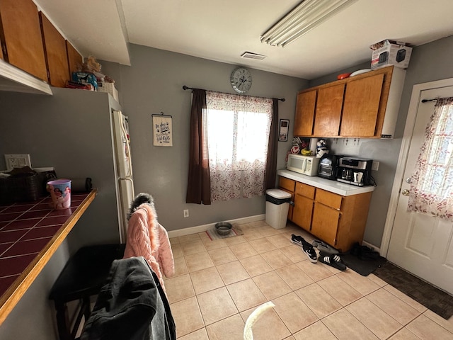 kitchen featuring brown cabinets, visible vents, tile countertops, and white microwave