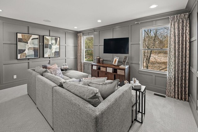 living room with a healthy amount of sunlight, visible vents, a decorative wall, and light carpet