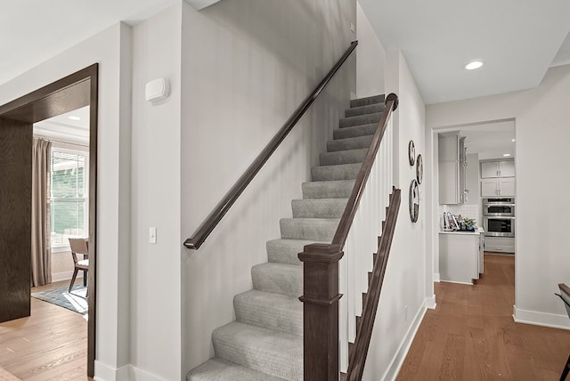 stairway with baseboards, wood finished floors, and recessed lighting