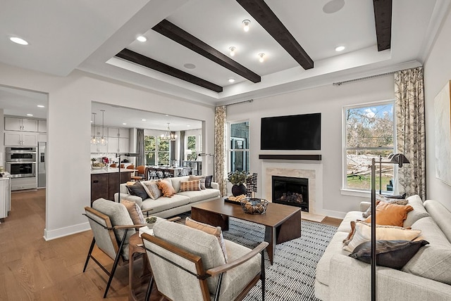 living room with a high end fireplace, baseboards, light wood finished floors, beamed ceiling, and an inviting chandelier