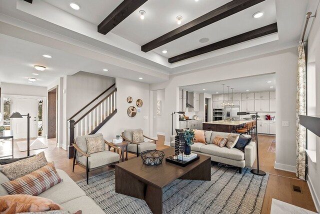 living room featuring visible vents, baseboards, stairway, light wood-type flooring, and beamed ceiling
