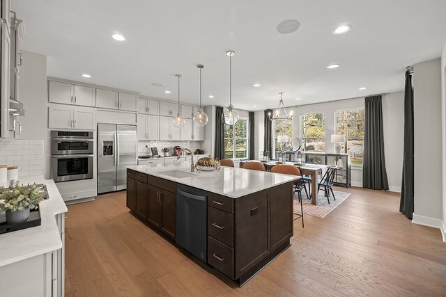 kitchen featuring light countertops, appliances with stainless steel finishes, dark brown cabinetry, a sink, and an island with sink
