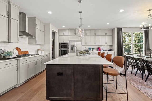 kitchen with a center island with sink, wall chimney exhaust hood, a breakfast bar area, light countertops, and pendant lighting