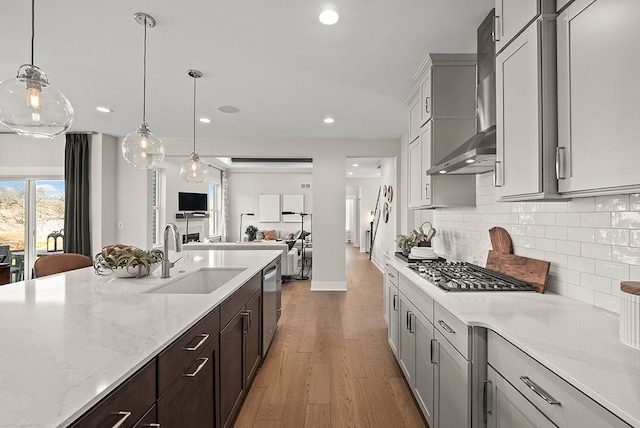 kitchen featuring appliances with stainless steel finishes, a sink, hanging light fixtures, and wall chimney exhaust hood