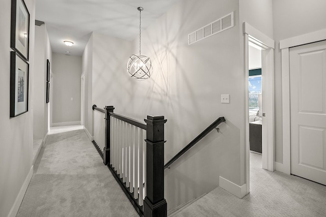 hall with baseboards, visible vents, light carpet, and an upstairs landing