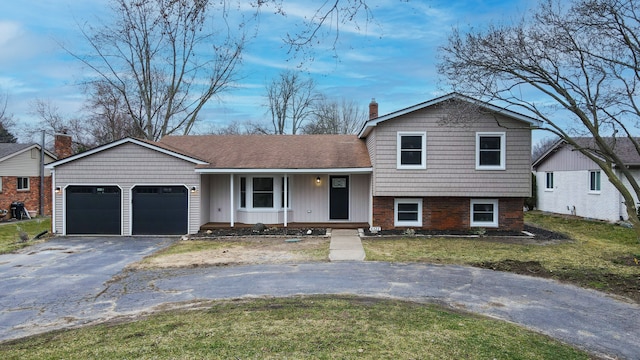 tri-level home featuring aphalt driveway, a chimney, a porch, an attached garage, and a front yard