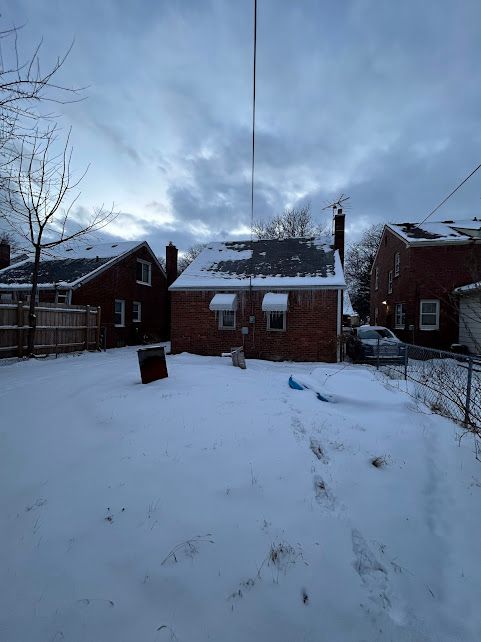 snow covered house featuring a chimney, fence, and brick siding