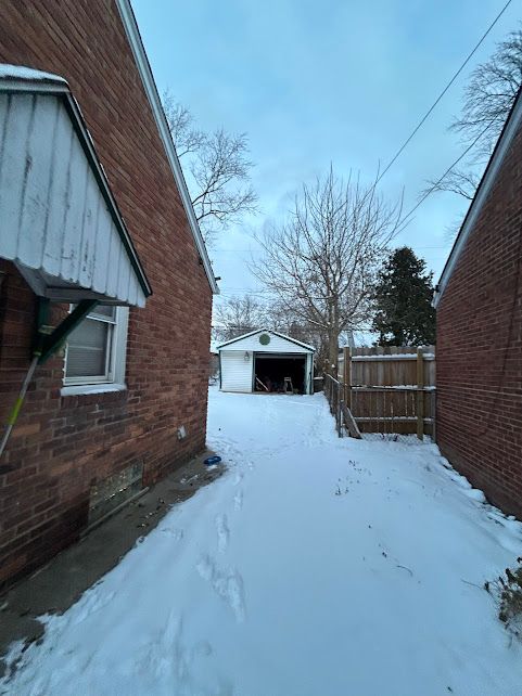 yard layered in snow with a detached garage, fence, and an outdoor structure