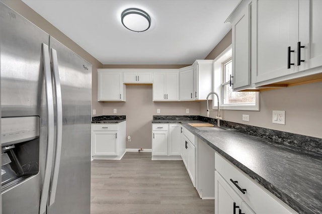 kitchen with dark countertops, stainless steel refrigerator with ice dispenser, a sink, and white cabinetry