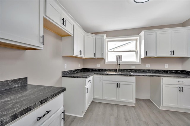 kitchen with dark stone countertops, a sink, light wood-style flooring, and white cabinetry