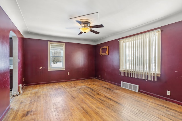 spare room featuring arched walkways, visible vents, hardwood / wood-style floors, ceiling fan, and baseboards