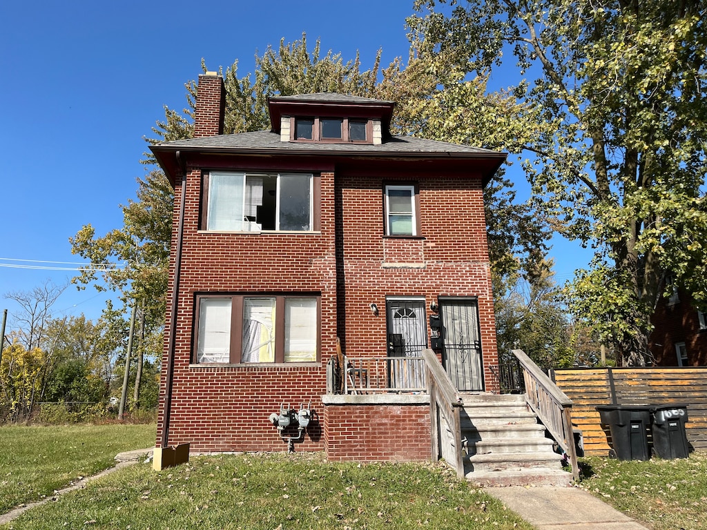 american foursquare style home with brick siding, a chimney, and a front yard