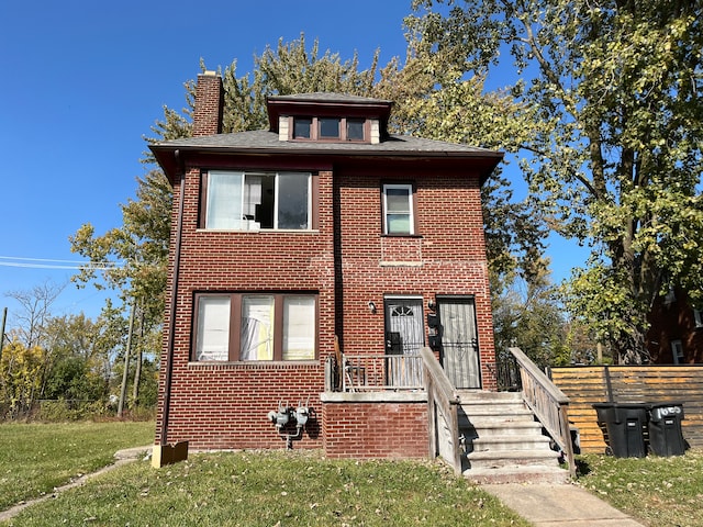 american foursquare style home with brick siding, a chimney, and a front yard