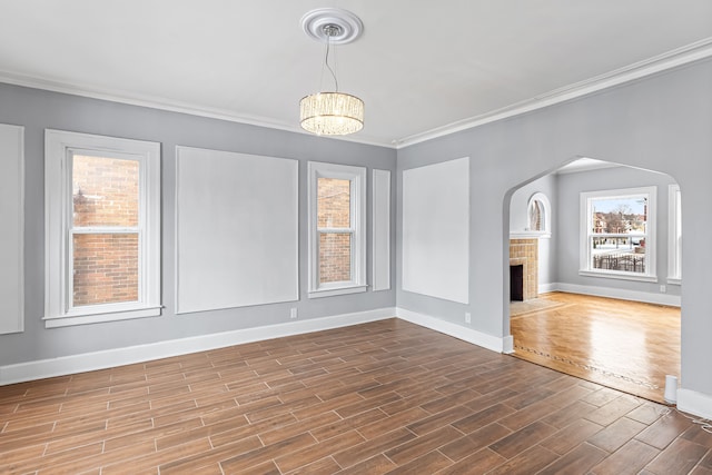 spare room with a healthy amount of sunlight, a fireplace, ornamental molding, and wood finished floors