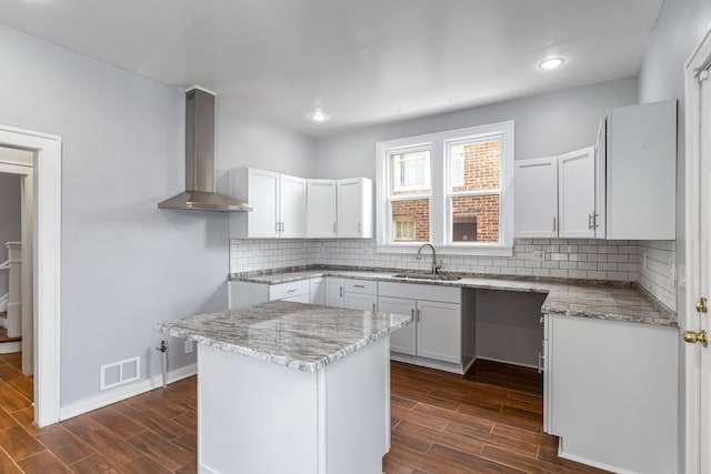 kitchen featuring a sink, visible vents, white cabinetry, wood tiled floor, and wall chimney exhaust hood