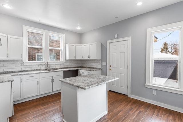 kitchen featuring a center island, white cabinets, a sink, and light stone countertops