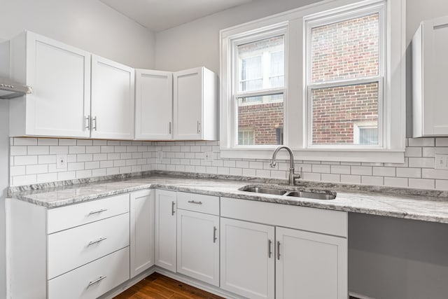 kitchen featuring dark wood-type flooring, a sink, light stone countertops, white cabinetry, and backsplash