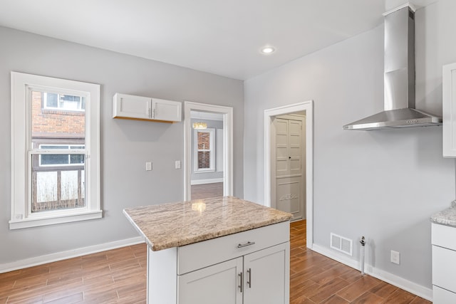 kitchen featuring visible vents, white cabinets, light stone counters, light wood-type flooring, and wall chimney range hood