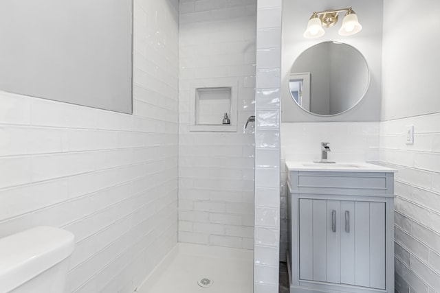 full bathroom with toilet, vanity, tile walls, wainscoting, and a tile shower