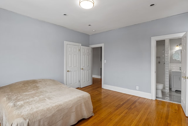 bedroom featuring baseboards, wood finished floors, and ensuite bathroom