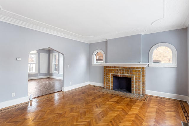 unfurnished living room featuring a wealth of natural light, arched walkways, crown molding, and a tiled fireplace