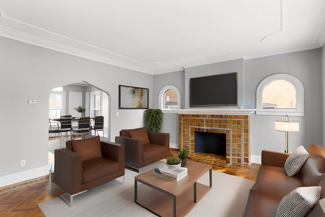 living area with baseboards, a tiled fireplace, arched walkways, and crown molding