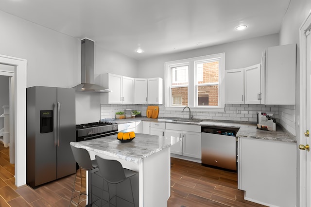 kitchen with white cabinets, appliances with stainless steel finishes, a center island, wall chimney range hood, and a sink