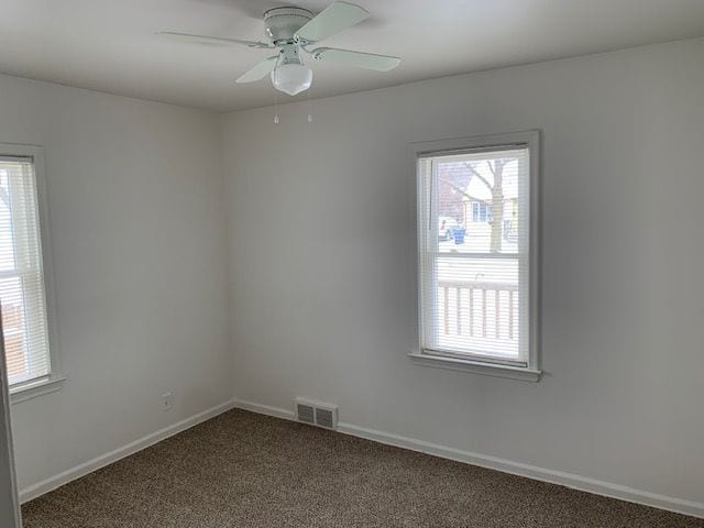 carpeted spare room with baseboards, visible vents, and ceiling fan