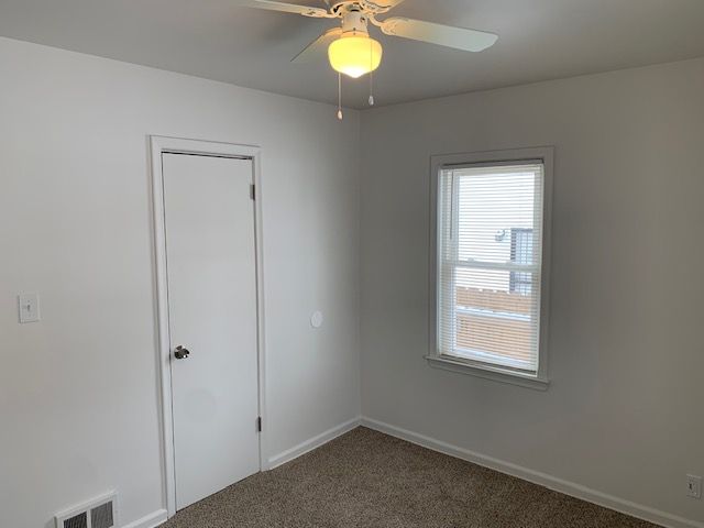 carpeted empty room with a ceiling fan, visible vents, and baseboards